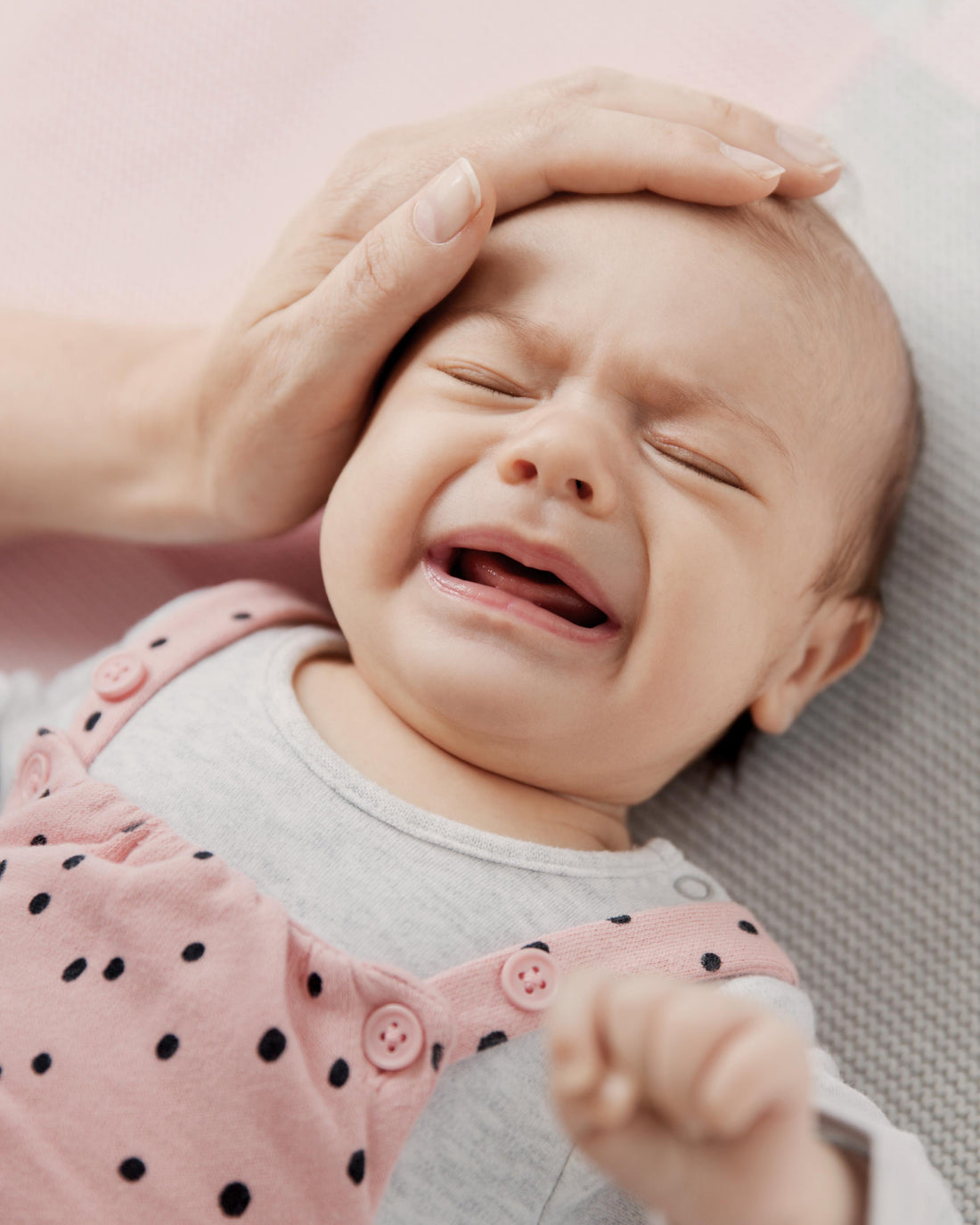 Mother gently touching her crying baby's hand