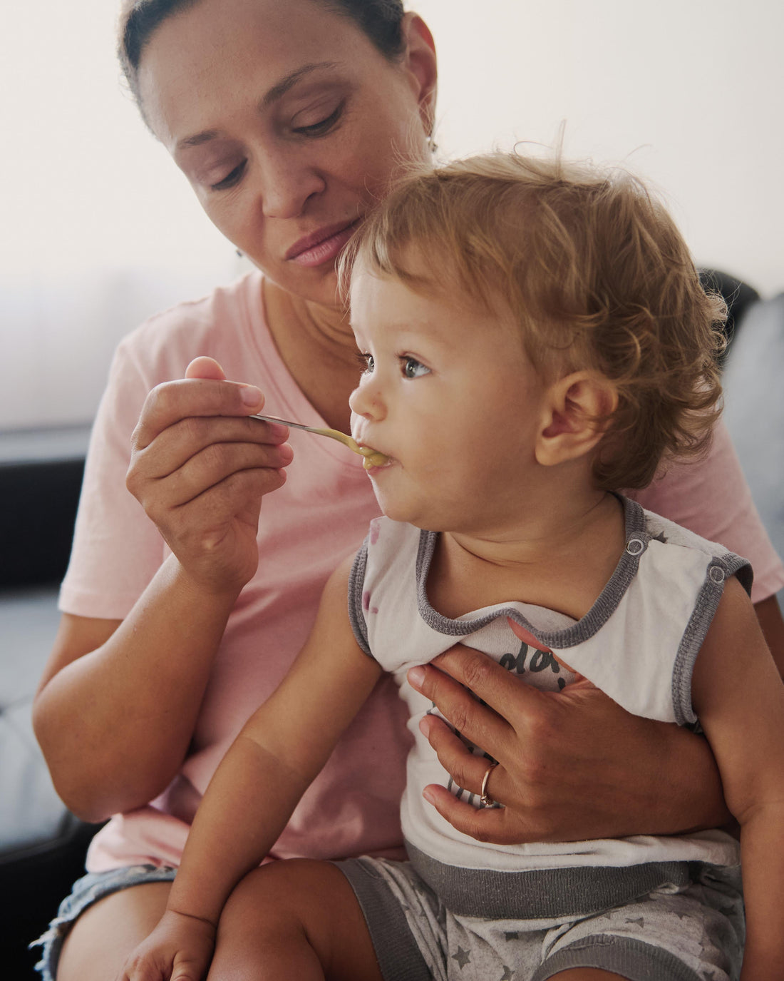 Mother feeding her toddler on the couch at home