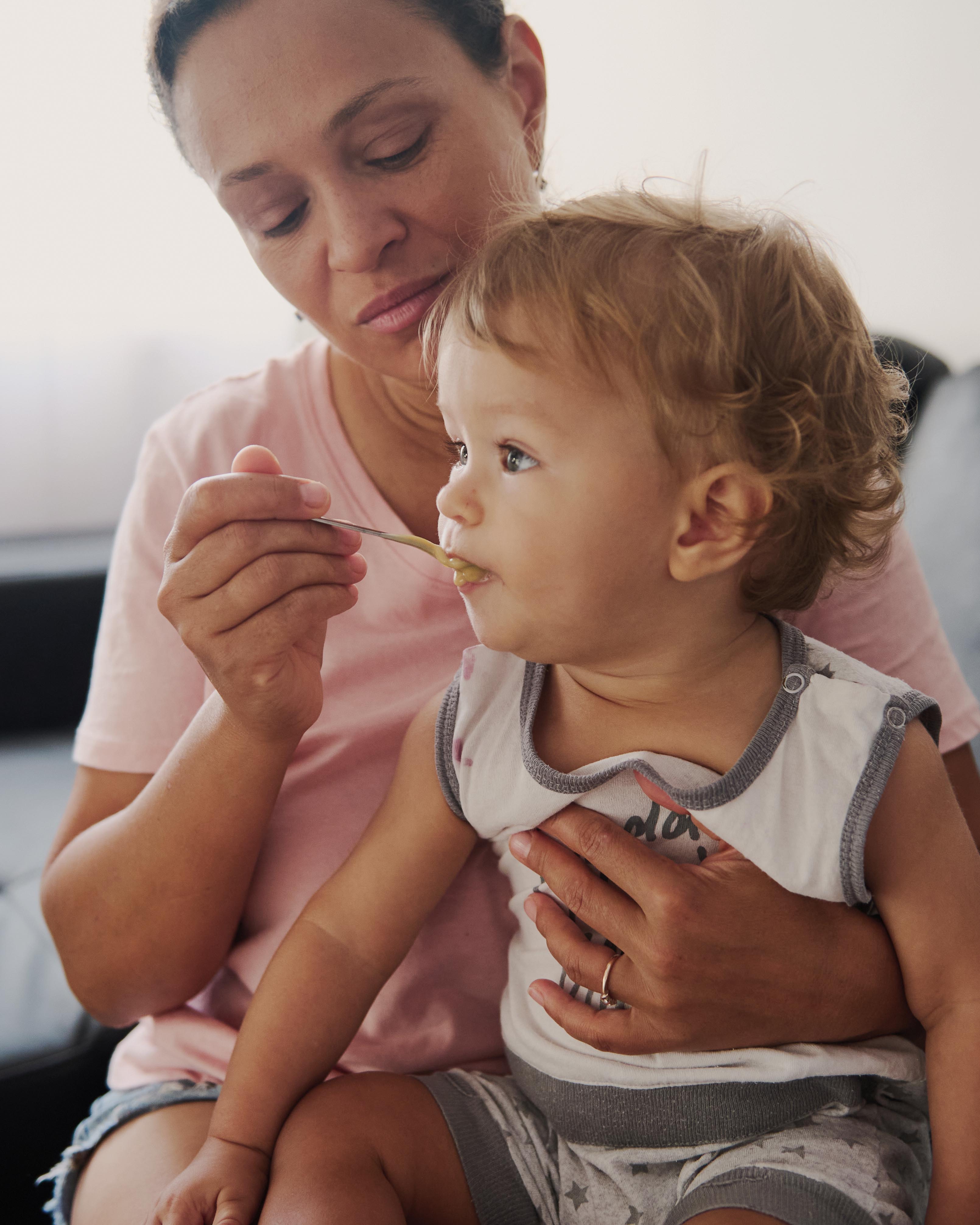 Mother feeding her toddler on the couch at home