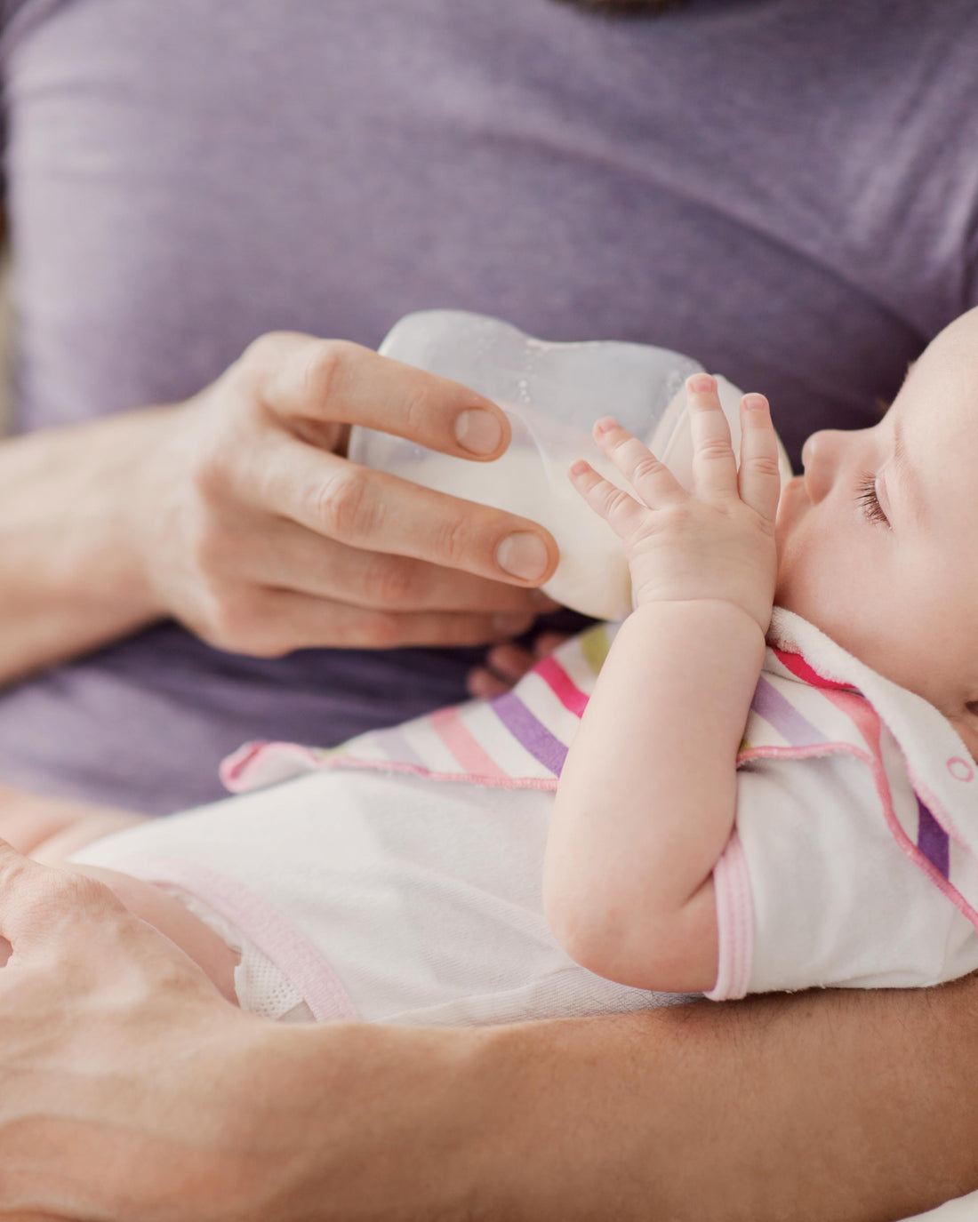 Father feeding his baby daughter with a bottle at home