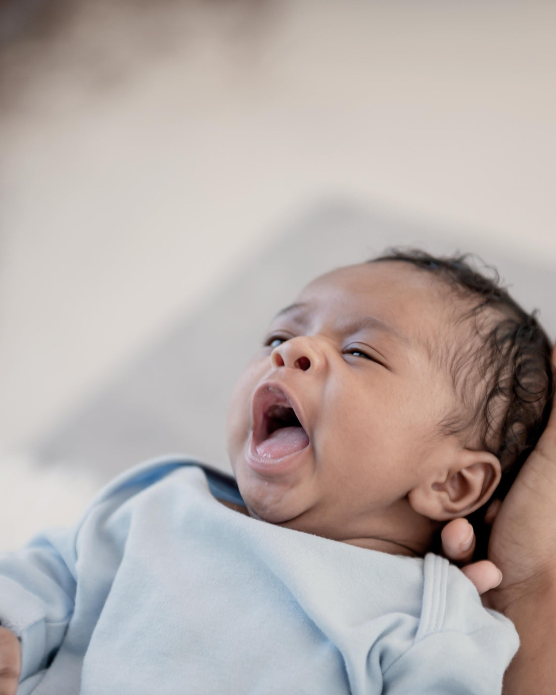 Newborn baby yawning sleepily on mother's arm