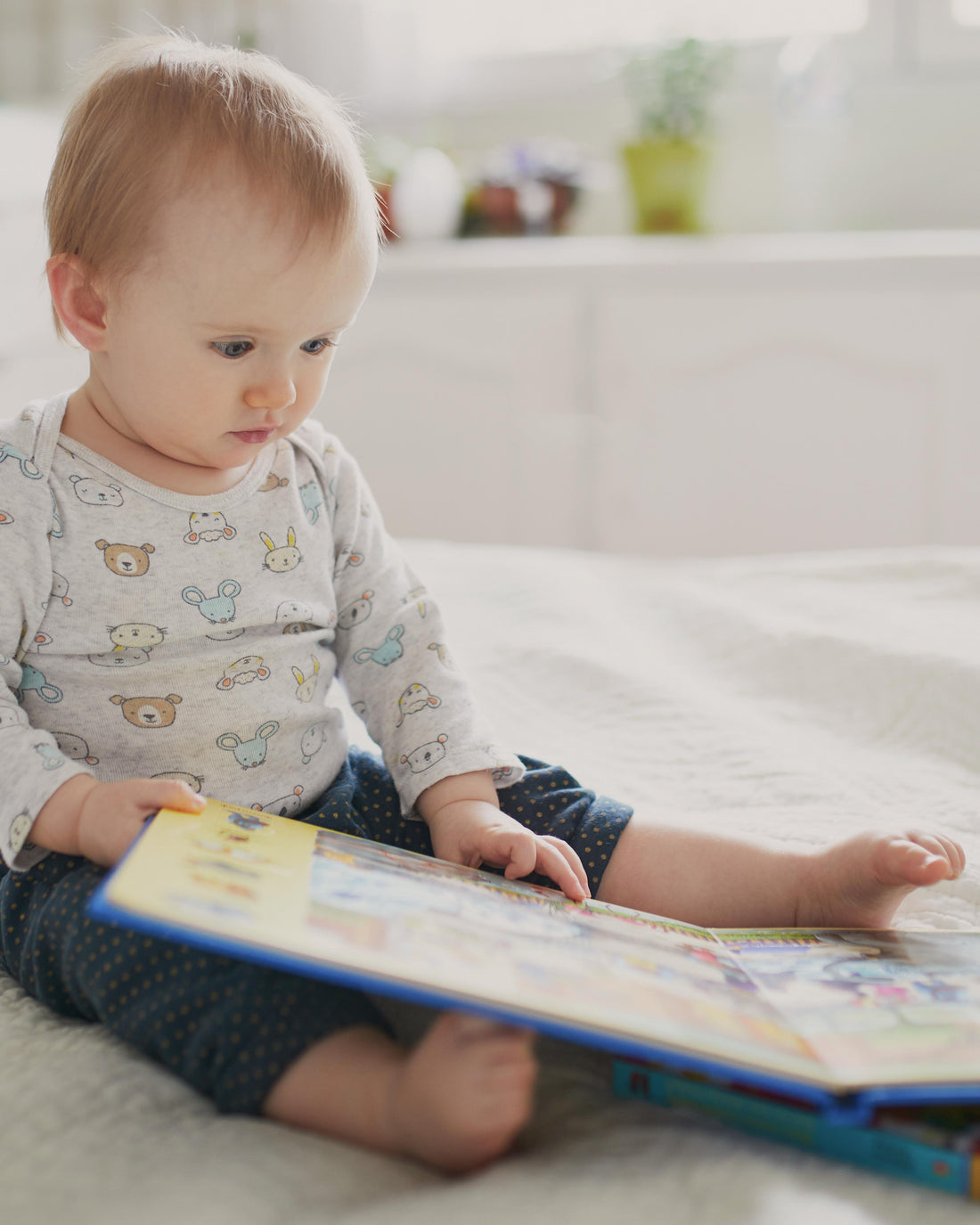 Baby girl reading a book while sitting on her bed