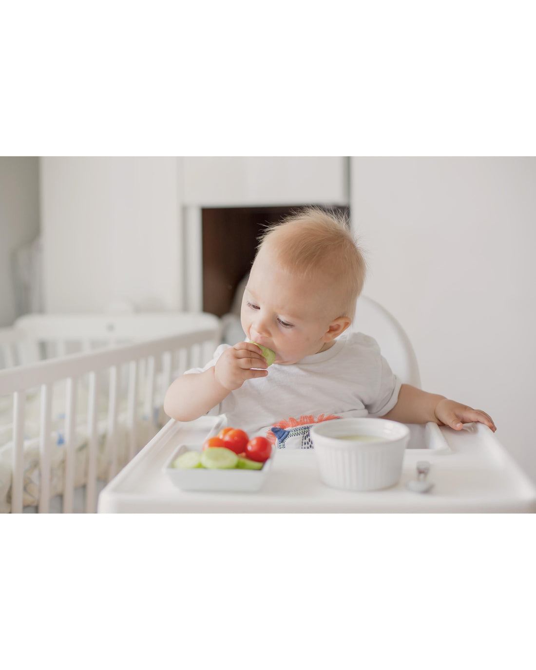 Baby self-feeding real foods in a high chair during a calm baby-led weaning activity